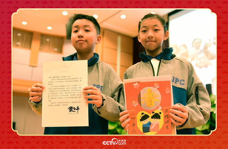 图为香港“少年警讯”成员郭宏晞(左)展示习主席回信、罗颢凝(右)展示送给习主席的贺卡并合影。