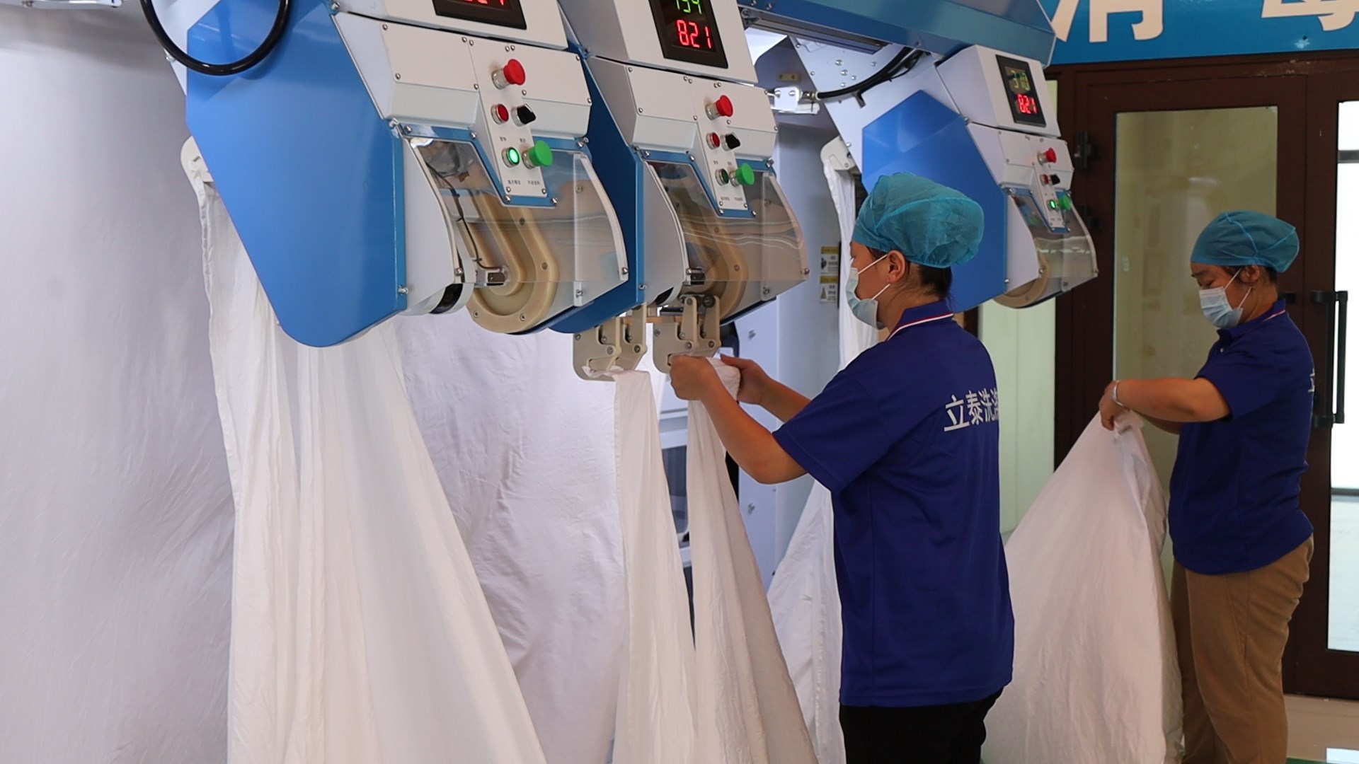 工作人员将洗净的布草挂上高速双面熨平机。